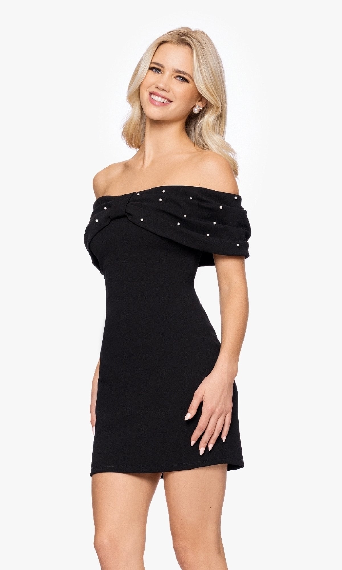 A woman stands and smiles against a plain background, wearing the Blondie Nites BC174 Off-Shoulder Black Hoco Dress featuring a pearl-beaded neckline.